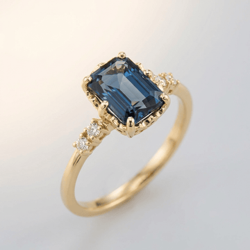 Anel de ouro com safira azul e detalhes em diamante, da marca Rose & Oliver, exibido em fundo neutro.
